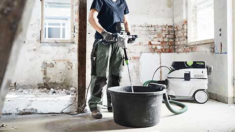 Uma artesã está no canteiro de obras e usa um misturador Festool em combinação com um aspirador.