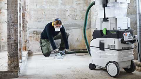Um artesão está a lixar um chão e a utilizar o sistema de lixamento de pisos Festool com aspiração.