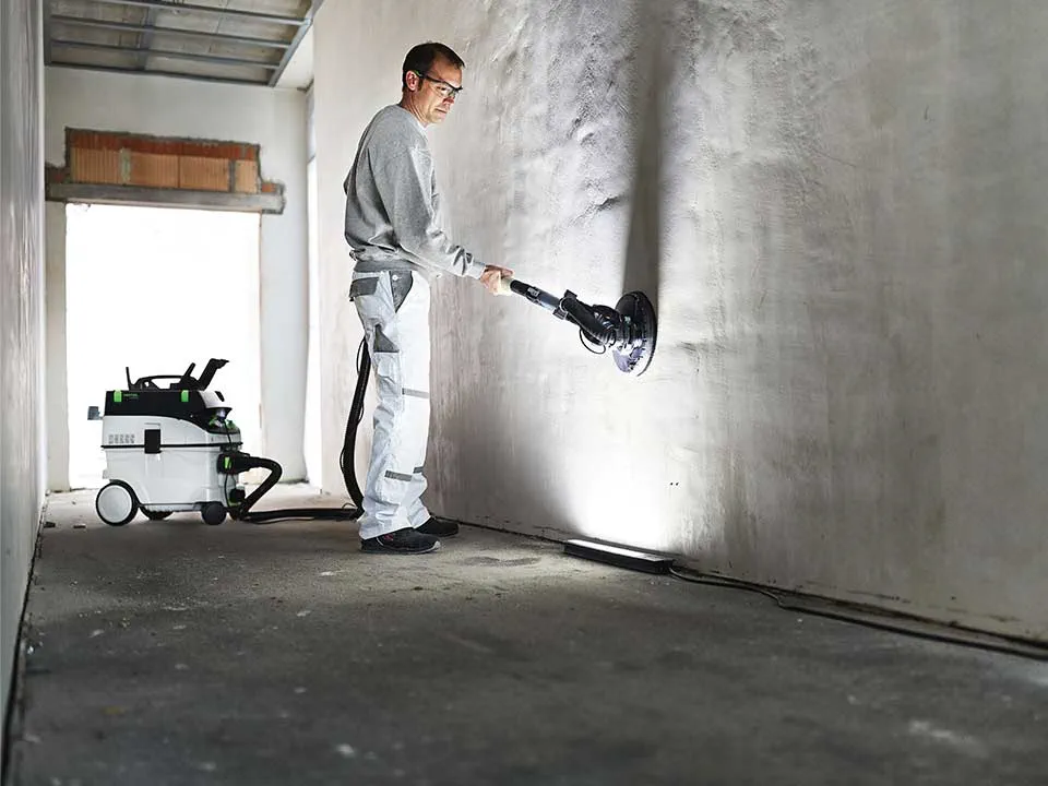 Um artesão ilumina uma parede com a ajuda da Luz rasante do pintor e lixa-a